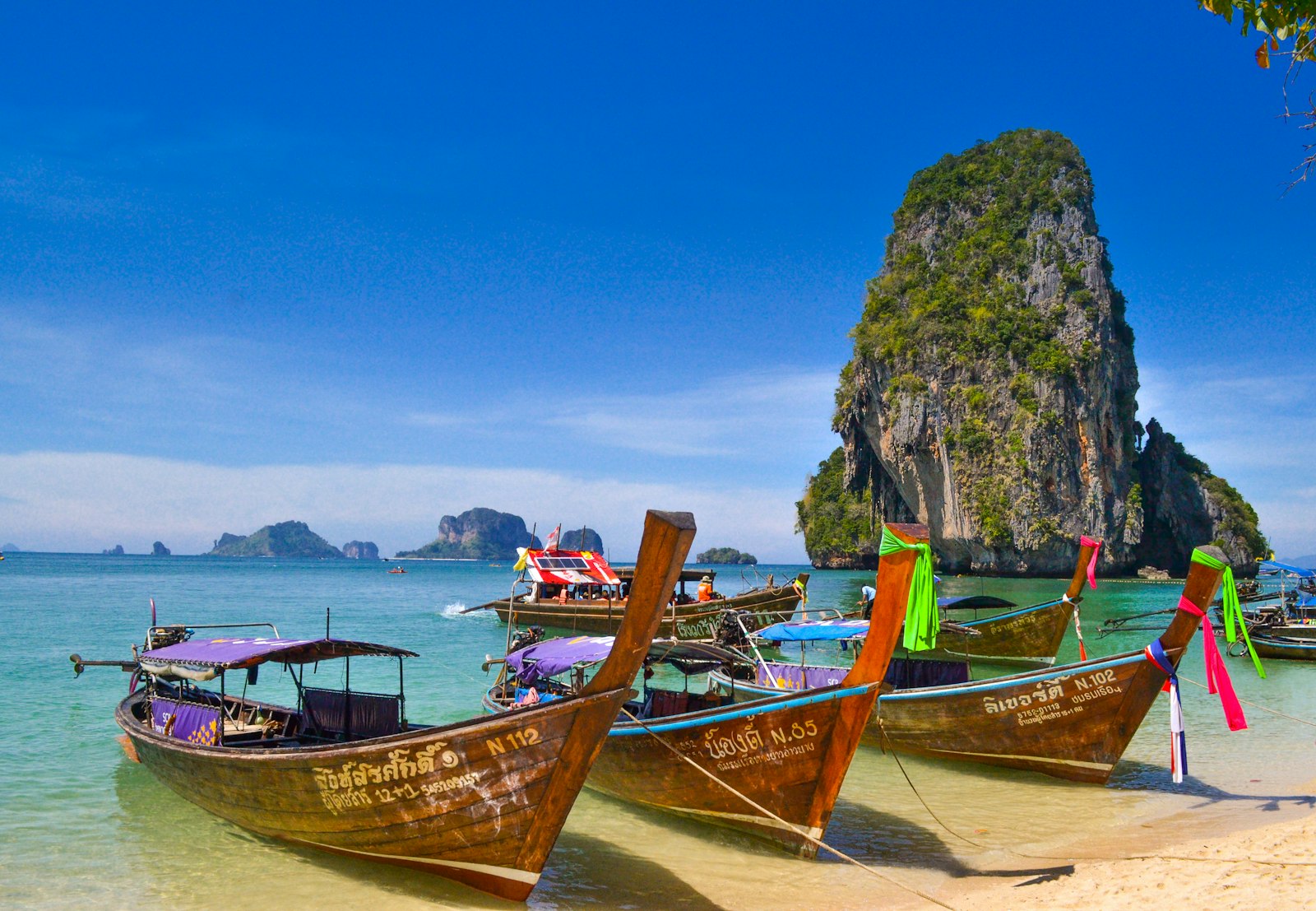 Long-tail boats in turquoise water beside limestone cliffs in Thailand
